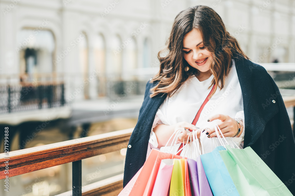 Happy young woman in casual clothing with shopping bags, at shopping mall.  Pluse size model in sales, shop, retail. Portrait of a happy girl after a  successful purchase. Stock Photo | Adobe