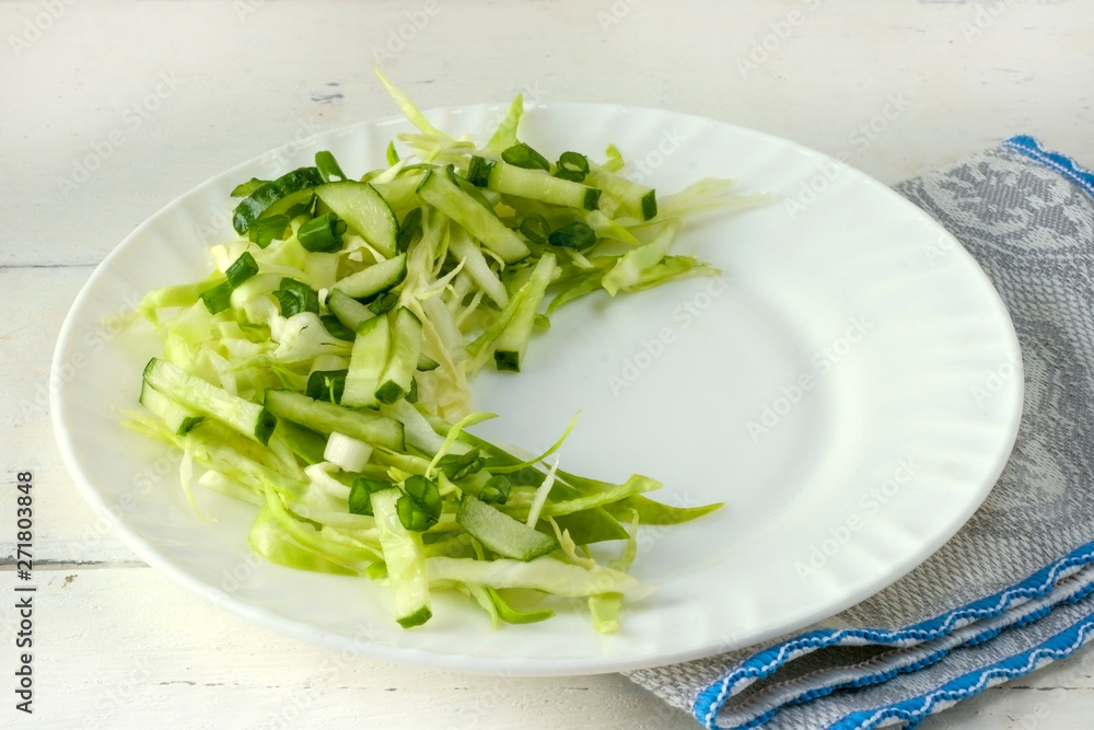 Spring vegan salad with cabbage, cucumber, green onions and parsley on a white plate Spring vegan salad with cabbage, cucumber, green onions and parsley on a white plate