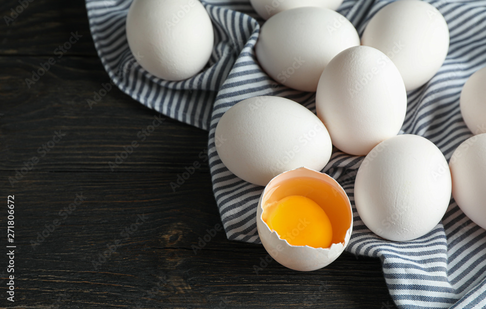 White chicken eggs in carton box and kitchen towel on wooden table, space for text and closeup White chicken eggs in carton box and kitchen towel on wooden table, space for text and closeup