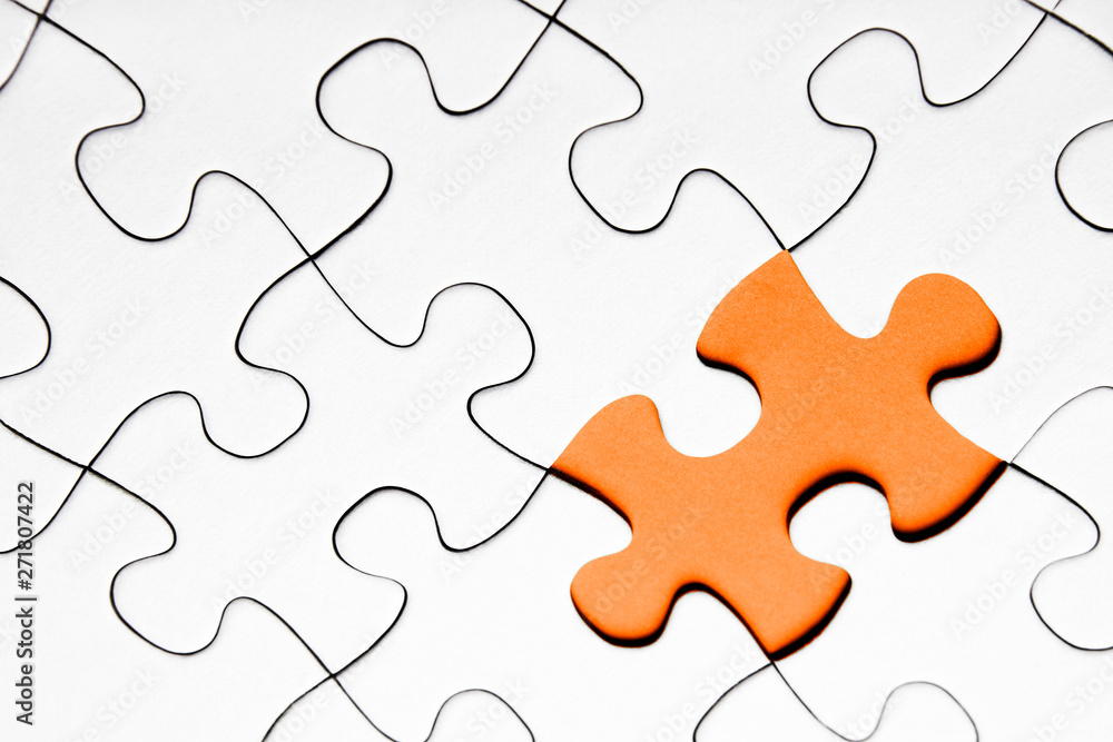 Orange puzzle piece in between of white puzzle pieces Orange puzzle piece in between of white puzzle pieces