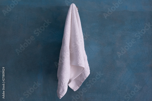 White towel hanging on ocean blue cement wall after shower.