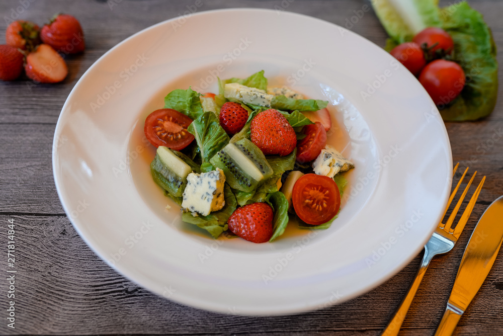 fruit and vegetable salad with strawberries, kiwi, cherry tomatoes and feta cheese in a white plate on a wooden table fruit and vegetable salad with strawberries, kiwi, cherry tomatoes and feta cheese in a white plate on a wooden table