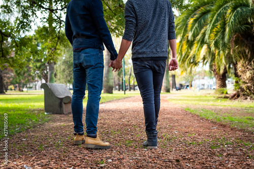 portrait without head of young gay couple holding hands and walking in the park
