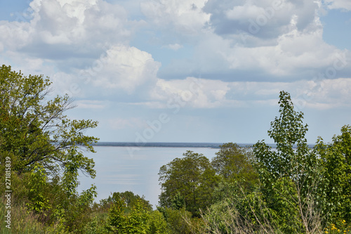 Landscape with green leafy trees, river and peaceful sky