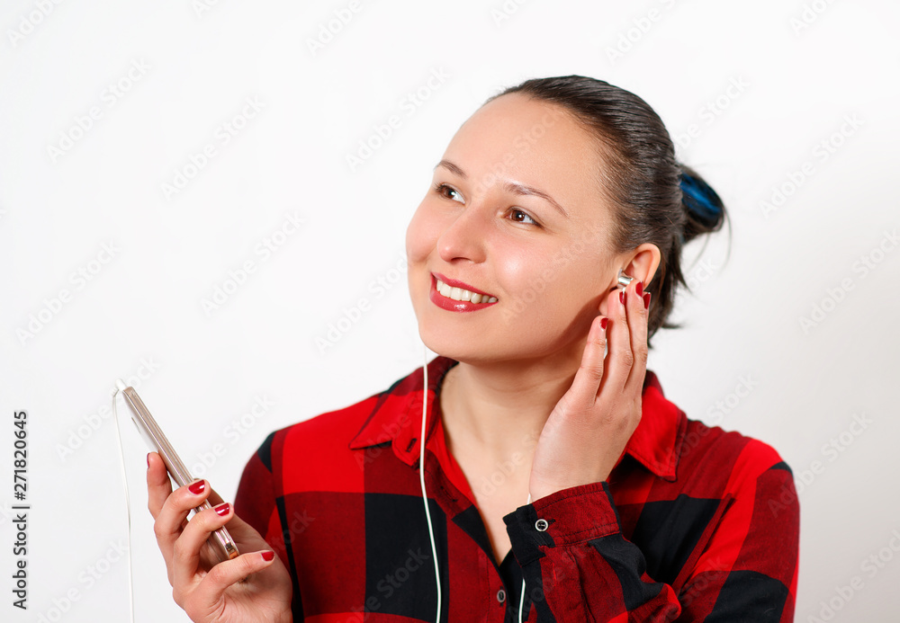 Obraz premium Happy young beautiful girl in red plaid shirt listening to music in headphones and smiling. On white background