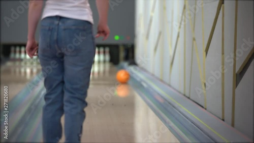 A woman in blue jeans and a white t-shirt is bowling: she throws an orange bowling ball with her right hand,the ball moves off the track, the average plan