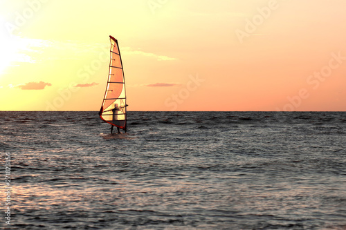 the person on a windsurf floats on water at sunset
