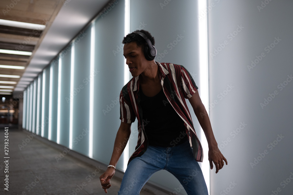 attractive young handsome guy walks in the neon light of the night city listens to music in wireless headphones from a mobile phone and dances fun