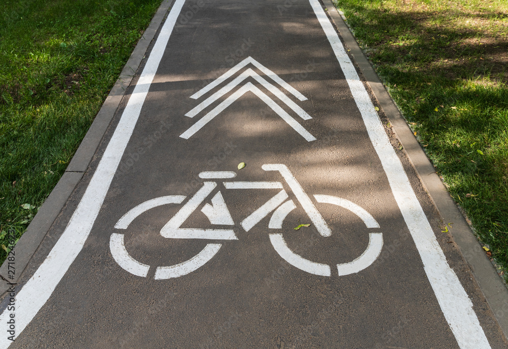 Obraz premium A Bicycle sign and an arrow with the direction of movement are drawn on the asphalt path
