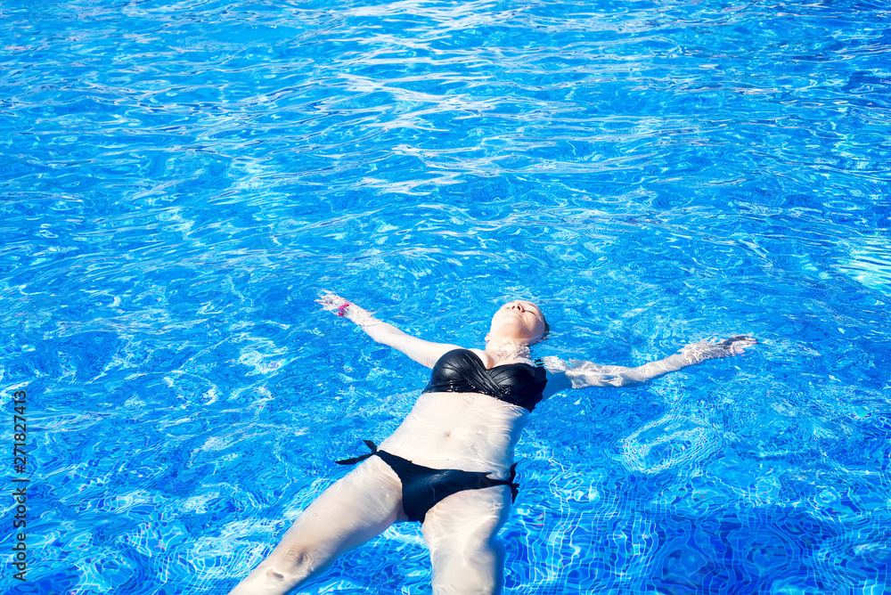 woman with black swimsuit swimming on a blue water pool, tropical vacation holiday concept