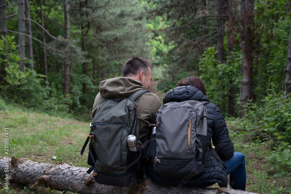 Couple of hikers sitting on a fall pine tree in the forest. Rear view Couple of hikers sitting on a fall pine tree in the forest. Rear view