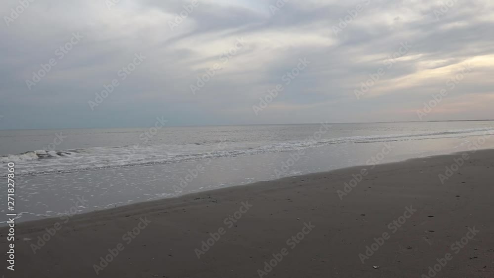 Waves gently crashing onto a sandy beach as sun sets over the horizon Waves gently crashing onto a sandy beach as sun sets over the horizon