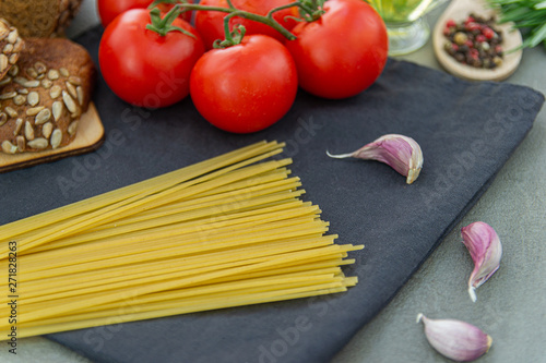 Ingredients For Italian pasta - spaghetti, ripe tomatoes, Basil, rosemary, spices and garlic. Gray background.