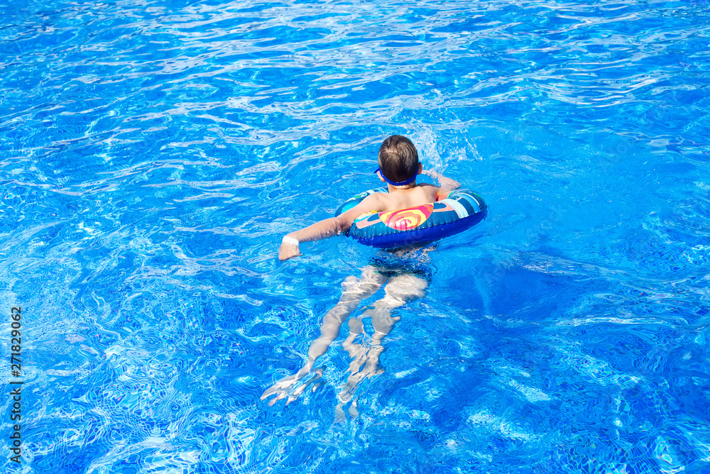 Happy cute little boy lying on an circle in the swimming pool. Cool summer holidays for children and kids. Active games on the water.