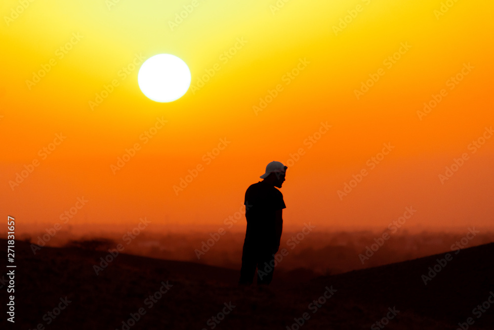 Silhouette of a man standing at the top of the mountain and looking at the sunset