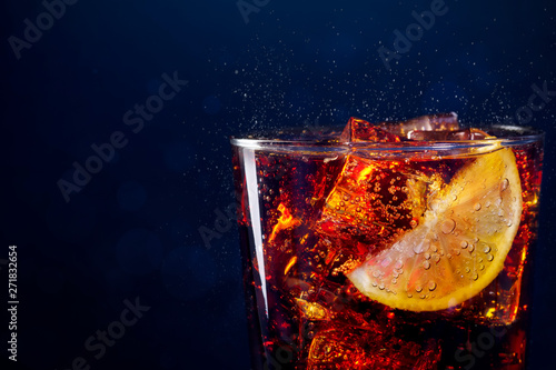 Close up to glass with drink and sliced citrus ice cubes. Close up to clear glass of fresh and appetizing drink with ice cubes and citrus slices on blue background.
