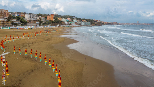 Aerial view of the coast of Anzio, a small sea town near Rome, in Italy. There is no one on the beach on this cold spring day. The blue sea with its waves is rough. In the sky there are some clouds. photo