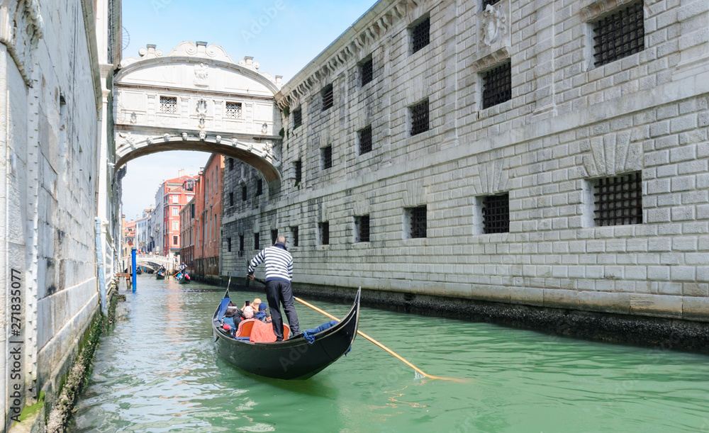 Gondolier punting gondola through green canal in Venice.