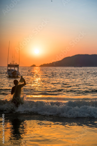 Fototapeta Naklejka Na Ścianę i Meble -  Silhouette of fisherman boy at sunset on the beach and boat background