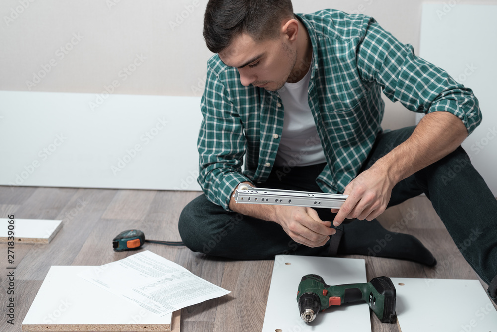 Large portrait of a man sitting on the floor of the room with tools collect furniture according to instructions Large portrait of a man sitting on the floor of the room with tools collect furniture according to instructions