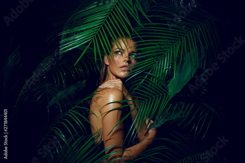 A beautiful tanned girl with natural make-up and wet hair stands in the jungle among exotic plants