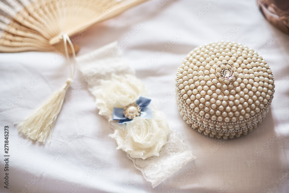 Close-up of white garter and wedding ring on white background.