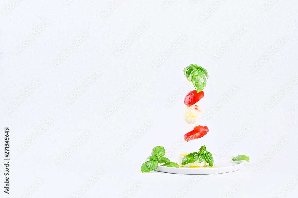 Flying salad in the frame. Traditional Italian caprese salad. Tomatoes, mozzarella, basil, olive oil on a white background. Flying salad in the frame. Traditional Italian caprese salad. Tomatoes, mozzarella, basil, olive oil on a white background.
