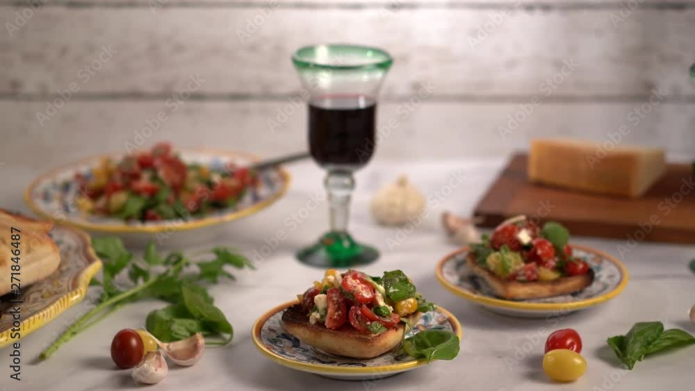 Trucking shot to the left with focus on a serving of bruschetta with tomatoes, basil, and mozzarella cheese with professional lighting. Trucking shot to the left with focus on a serving of bruschetta with tomatoes, basil, and mozzarella cheese with professional lighting.