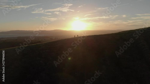 Two people standing on top of a mountain as a drone flies over towards a beautiful countryside sunset photo