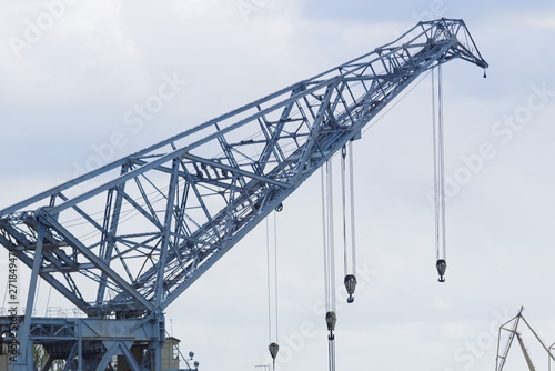 The arrow of a huge port crane with a lot of cables and hooks against the cloudy sky