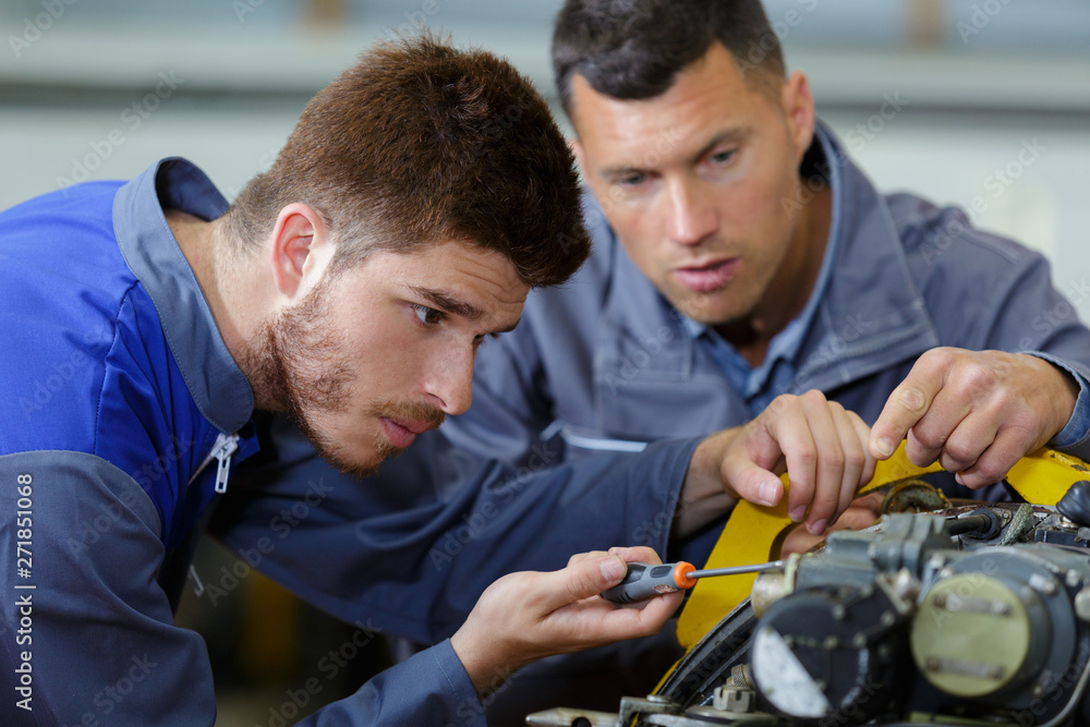 male apprentice engineer using screwdriver under supervisors guidance male apprentice engineer using screwdriver under supervisors guidance