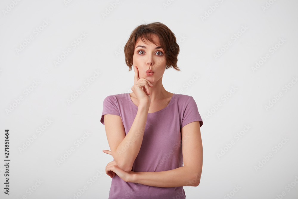 Young attractive young short-haired woman in blank t-shirt with a surprised expression on her face, isolated over white wall. Young attractive young short-haired woman in blank t-shirt with a surprised expression on her face, isolated over white wall.