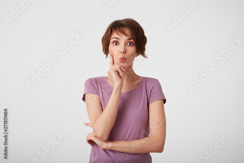 Young attractive young short-haired woman in blank t-shirt with a surprised expression on her face, isolated over white wall.