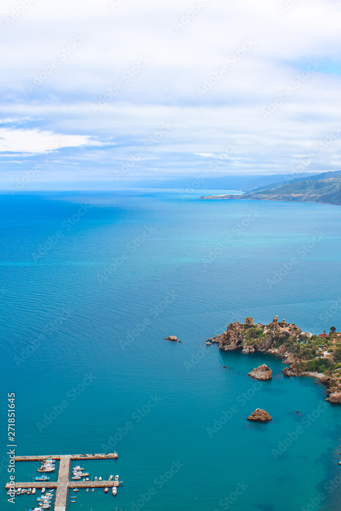 Dark blue calm water of Tyrrhenian sea surrounding the Sicilian coastal village Cefalu from above. Captured on vertical picture with pier and boats in the sea