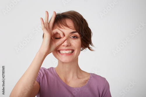Wallpaper Mural Close up of young attractive happy short-haired lady in blank t-shirt, standing over white wall and looking through okay gesture and broadly smiling Positive emotion concept. Torontodigital.ca