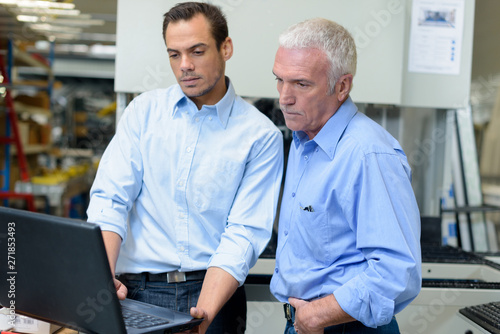 two management level workers looking at laptop in factory