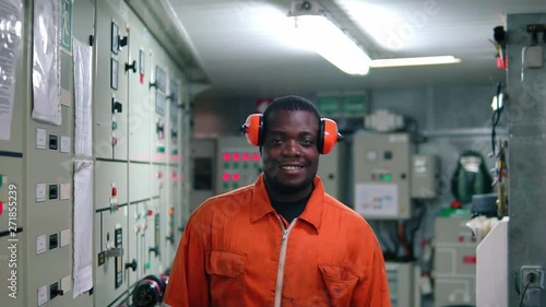 African marine engineer officer in engine control room ECR. He walks and looks at the camera photo