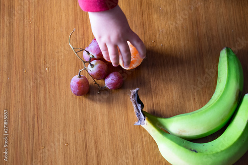 Baby s hand manipulating different fruits on a wooden table photo