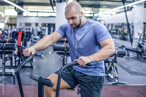 young athlete using exercise bike at the gym. Fitness male using air bike for cardio workout at crossfit gym and listenin music. dressed in sportswear