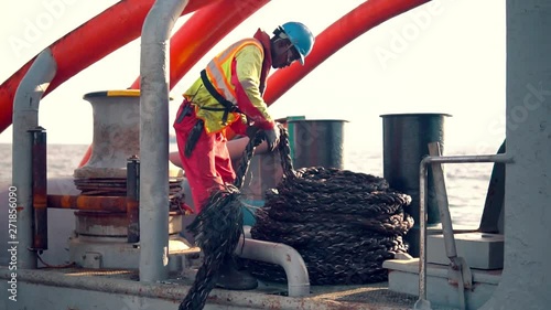 Seaman AB or Bosun on deck of vessel or ship , wearing PPE personal protective equipment - helmet, coverall, lifejacket, goggles. He coils mooring rope