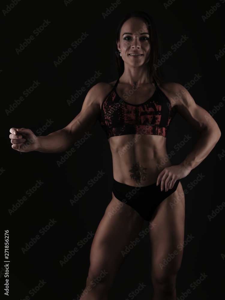 Fototapeta premium Sporty woman does the exercises on black background