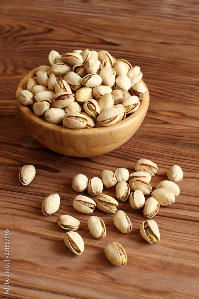 Salted dried pistachio nuts in bamboo bowl on wooden background Salted dried pistachio nuts in bamboo bowl on wooden background