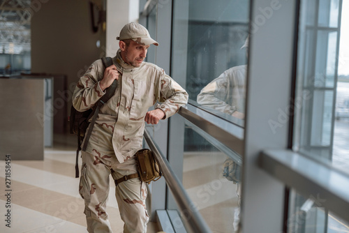 Waist up of calm American soldier in camouflage standing at the window