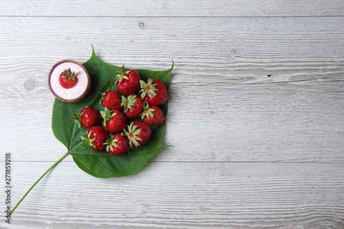 Homemade yogurt with fresh strawberry on a wooden background and few organic strawberries on a big green leaf
