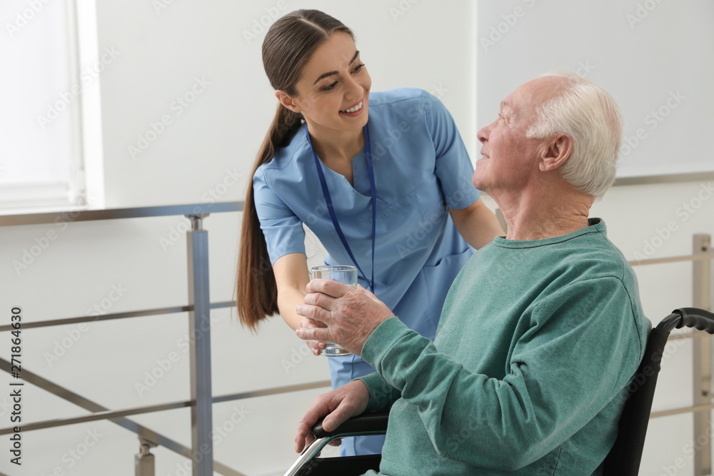Obraz premium Nurse giving water to senior man in wheelchair at hospital. Medical assisting