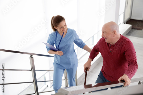 Nurse assisting senior man with cane to go up stairs indoors