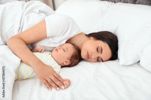 Mother and her cute baby sleeping on bed indoors