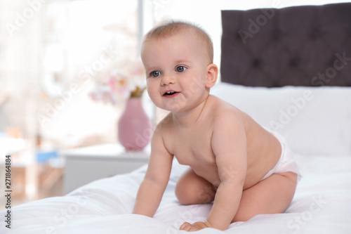 Cute baby in diaper on bed at home
