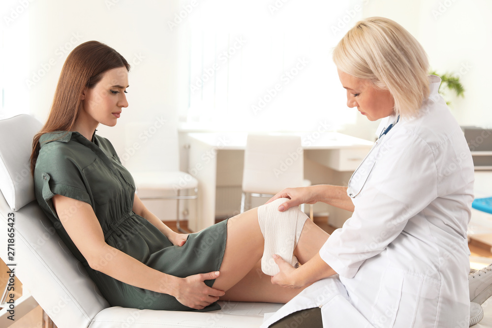 Doctor applying bandage to patient's knee in clinic