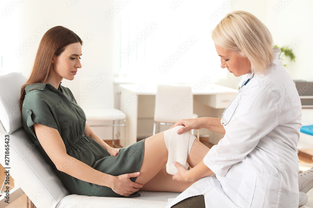 Doctor applying bandage to patient's knee in clinic Doctor applying bandage to patient's knee in clinic